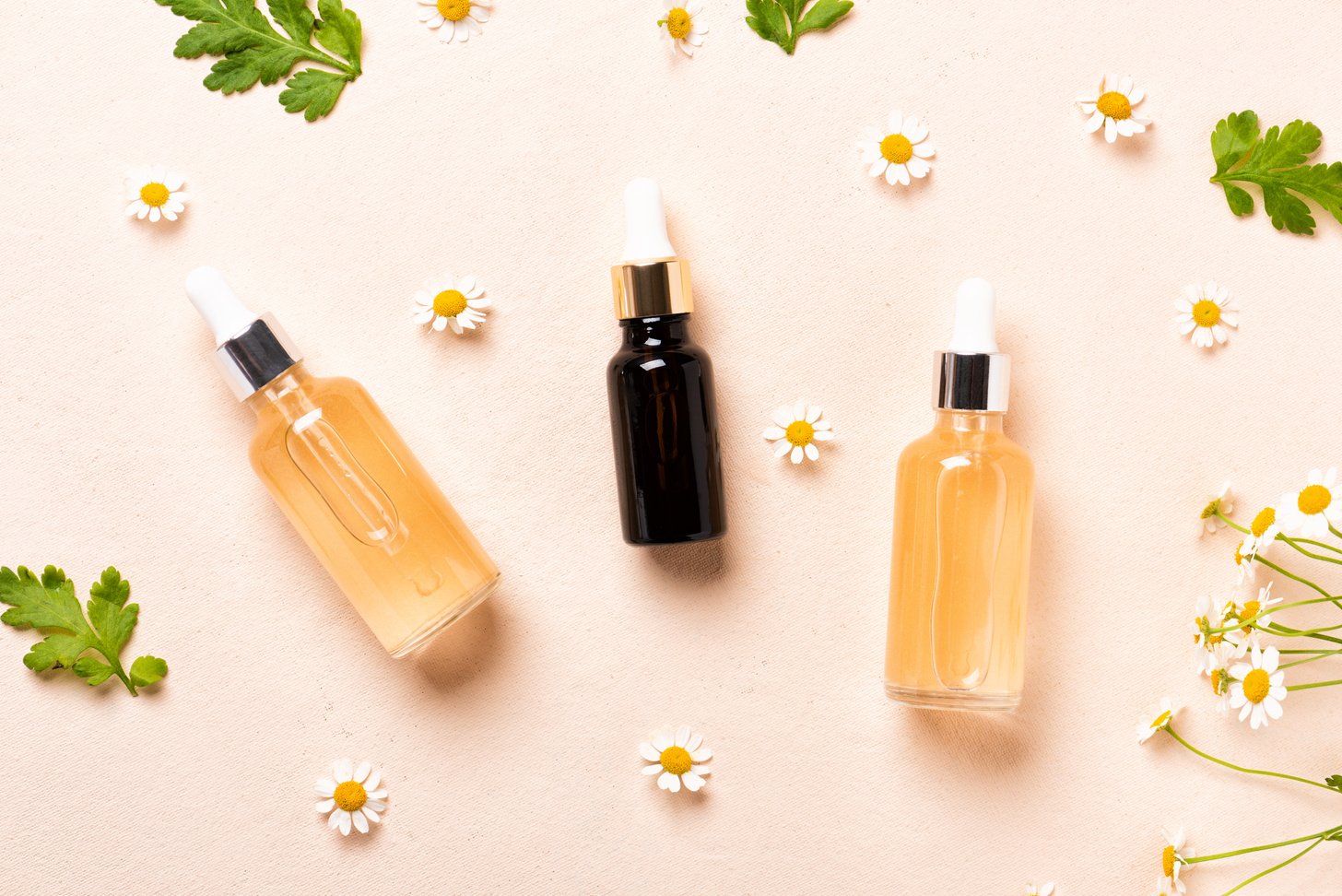 Glass bottles of essence or serum with chamomile flowers.